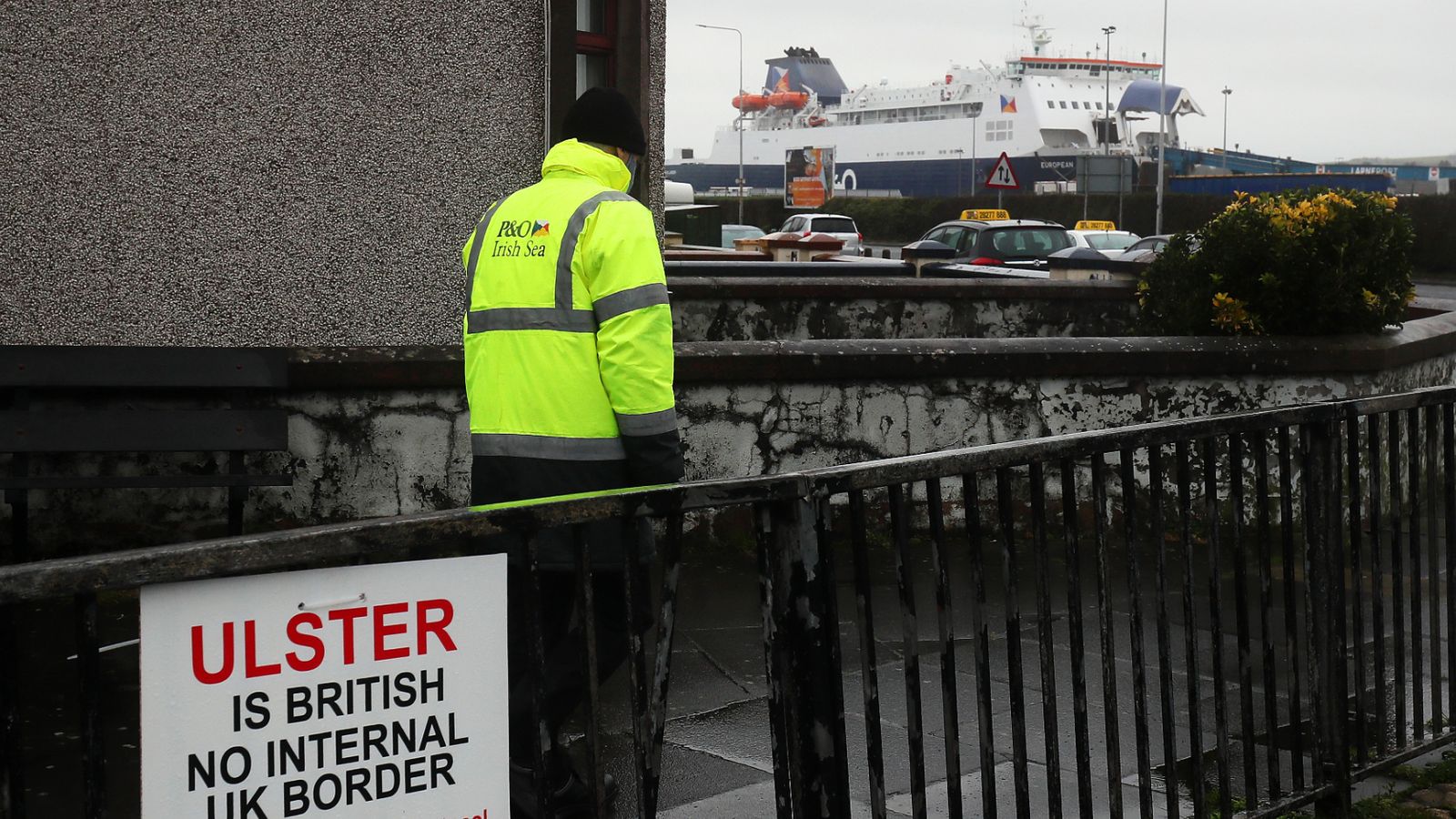 一个站在篱笆旁边的人：北爱尔兰拉恩港入口附近的反脱欧标志